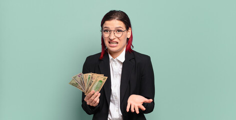 young attractive red hair woman looking angry, annoyed and frustrated screaming wtf or what’s...