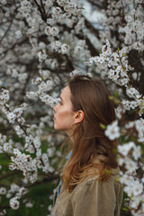a girl stands sideways in a garden or park near a blooming apple tree apricot tree in spring
