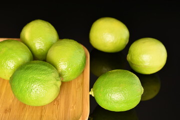 Several bright green juicy limes on a wooden dish, close-up, on a black background.