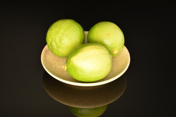 Three ripe lime on a saucer, close-up, on a black background.