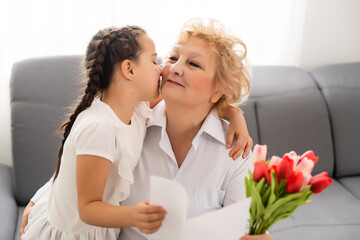 Nice little girl presenting bouquet to her grandmother in light room