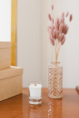 A candle, a vase of flowers, two boxes on a chest of drawers with a floor lamp in the interior. Home and interior concept.