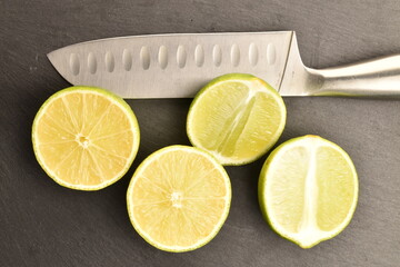 Four halves of natural lime with a knife, close-up, on a serving plate of slate.