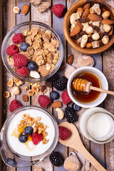 on the rustic wooden background, tasty and healthy breakfast with yogurt, cereals, dried fruit, raspberries, blueberries and blackberries, bowl with forest honey. view from top