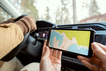 Hands of young woman sitting by driver and holding smartphone with map