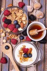 on the rustic wooden background, tasty and healthy breakfast with yogurt, cereals, dried fruit, raspberries, blueberries and blackberries, bowl with forest honey. view from top