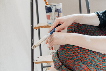 Person sits near stepladder, holding brush in hand and resting after painting the walls. Home Renovation Concept