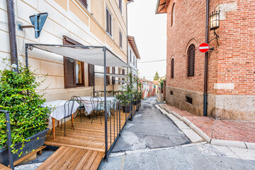 Fototapeta na wymiar Chiusi, Italy - August 25, 2018: Narrow alley road street with restaurant tables terrace in small town village in Tuscany and nobody