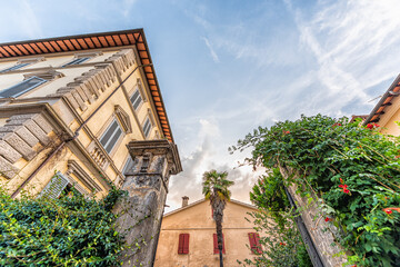 Fototapeta na wymiar Chiusi, Italy street in small historic medieval town village in Tuscany during summer day with nobody orange yellow house looking up wide angle view blue sky and palm tree