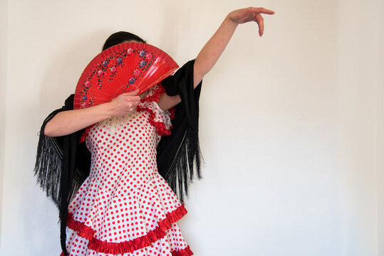 Hermosa mujer española con traje rojo de flamenca y mantón de manila negro sostiene un abanico rojo en una mano. Concepto de bailaora de sevillanas. Flamenco