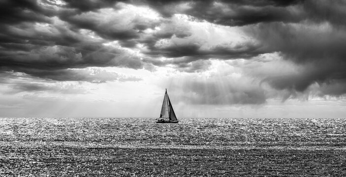 Black and white photograph of a sailboat sailing in a dramatic sunset