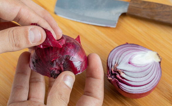 Hands peeling a piece of purple onion