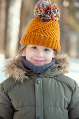 Adorable child in warm jacket and knitted brown beanie looking at you outside