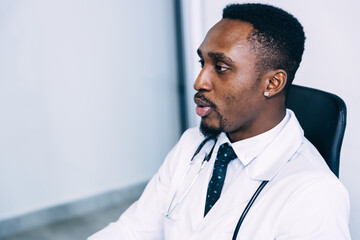 Portrait of an Afro-Mexican male doctor in a white coat with a stethoscope sitting at a desk in the office