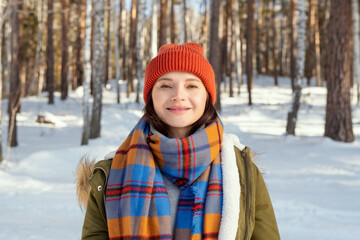 Fototapeta na wymiar Young cheerful woman in warm jacket, checkered scarf and beanie looking at you