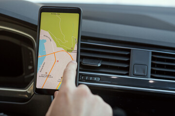 Hand of young man sitting in car and pointing at map on screen of smartphone