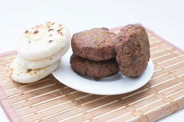 Seasoned meatloaf served with corn arepa on white wooden background