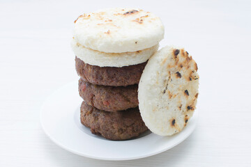 Seasoned meatloaf served with corn arepa on white wooden background