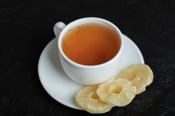 A cup of aroma tea with dried pineapple on a dark background