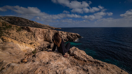 Girl sitting on the cliff at sunset time