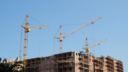 Working on place with many tall buildings under construction and cranes under a blue sky