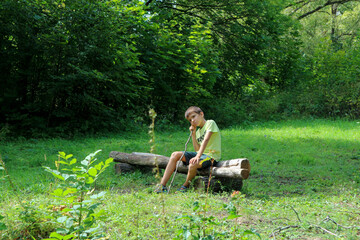 Naklejka na ściany i meble tired boy sitting on a wooden bench in a clearing in the forest 