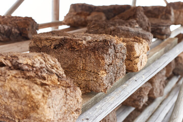 Three hunks of peat piled up for drying on wooden shelf with blurred background. Peat production