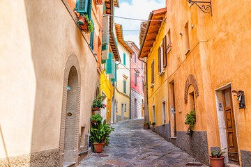 Chiusi, Italy narrow street alley in small historic medieval town village in Tuscany during sunny day with orange yellow multicolored colorful walls and nobody
