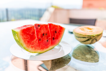 Summer day with vivid vibrant colorful red watermelon slice cut and honeydew melon outside in Italy on white plate and glass table with seeded black seeds