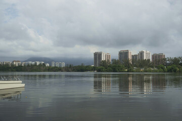 View of Marapendi Lagoon, with buildings and ferry boats in the background amid the exuberant nature of the place. Cloudy day with the stone of the crow covered by the clouds and fog. Located next to 