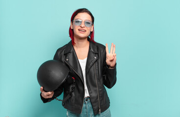 young attractive red hair woman smiling and looking friendly, showing number three or third with...