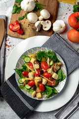 Fresh salad with lettuce tomato cucumber mushroom cheese and parsley top view over gray stone table 