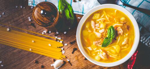 Chicken soup with noodles and vegetables in white bowl on wooden table background