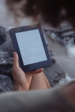Male hands holding an e-book, e-book, e-reader on a relaxing rocky beach.