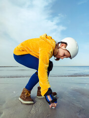 Portrait of pretty teenager girl in yellow pullover, helmet and inline protective equipment posing...