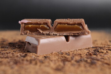 A cut of chocolate stuffed with caramel chocolate bar lies on the cocoa on a black background with place for text and a copy of the day of chocolate