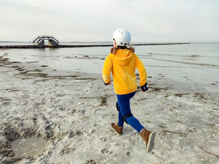 Happy child girl in yellow pullover in helmet and inline protective equipment running and having...