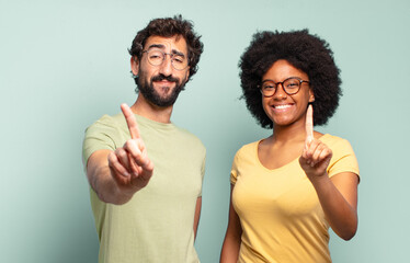multiracial couple of friends smiling proudly and confidently making number one pose triumphantly,...