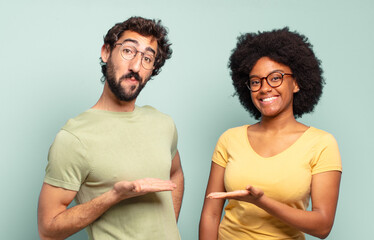 multiracial couple of friends smiling cheerfully, feeling happy and showing a concept in copy space...