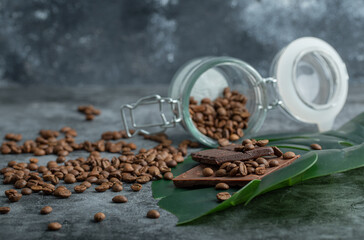 A glass jar full of coffee beans with chocolate bars on a gray background