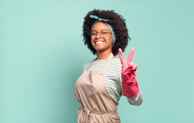 black afro woman smiling and looking happy, carefree and positive, gesturing victory or peace with...