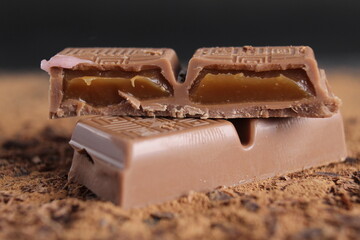A cut of chocolate stuffed with caramel chocolate bar lies on the cocoa on a black background with place for text and a copy of the day of chocolate