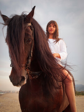 Joven amazona con vestido blanco domando a su caballo marron sin montura en la playa