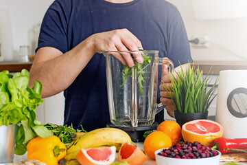 A man prepares a wellness food smoothie with fresh herbs, bananas and fresh berries in a blender 
