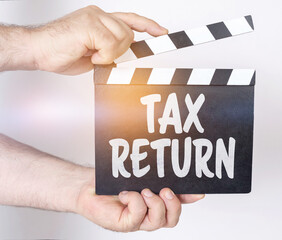 On a white background, a man holds a clapperboard in his hands on which it is written - TAX RETURN