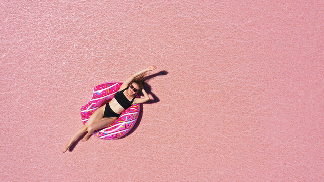 Aerial view of Beautiful woman lying in a bikini on inflatable mattress on pink salt lake. copy space. opening of the tourist season. summer holiday concept. taken from above from a drone