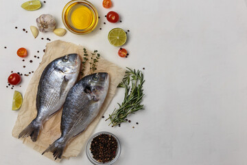Fresh fish dorado fish on baking paper on white table with ingredients for cooking