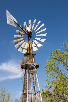 Old wind turbine with blue sky and trees in background
