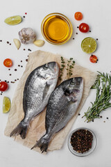 Fresh fish dorado fish on baking paper on white table with ingredients for cooking
