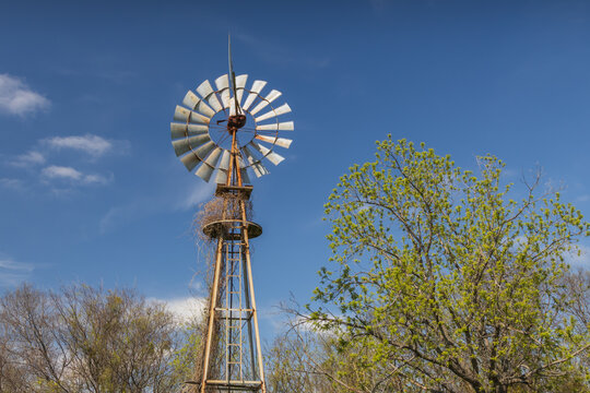 Old wind turbine with blue sky and trees in background

